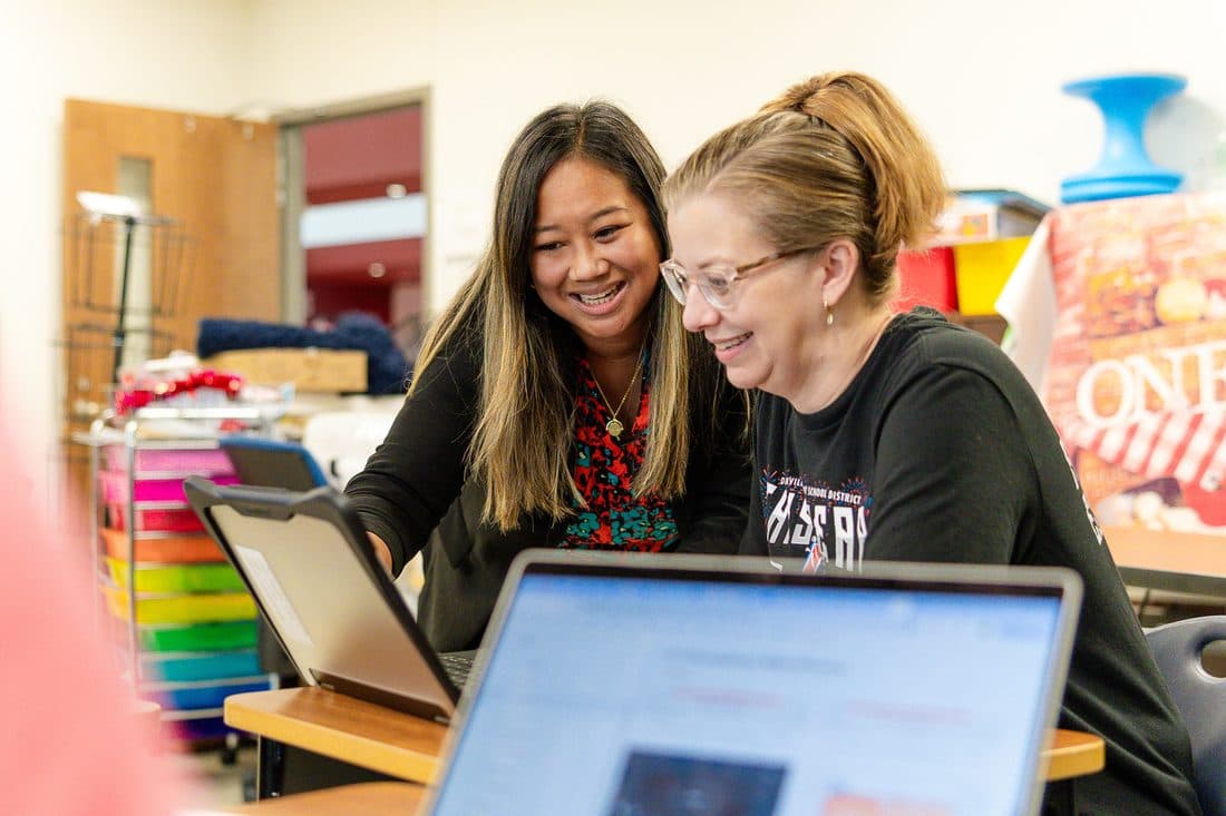 Two educators smiling while collaborating over a laptop in a classroom
